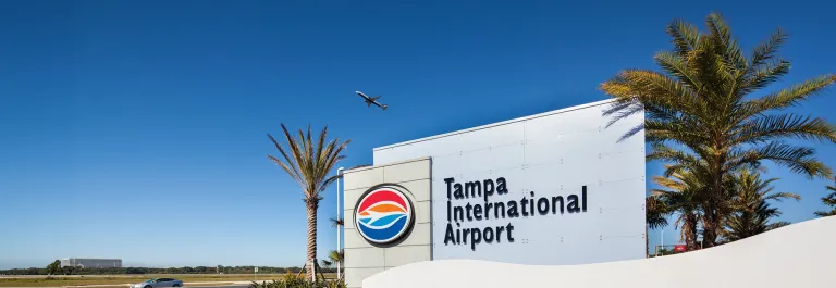 Large sign for Tampa International Airport with passenger jet taking off into a clear blue sky the background