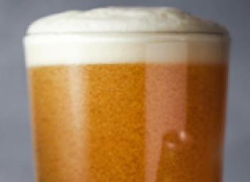 Top of a pint glass filled with beer with a foamy top