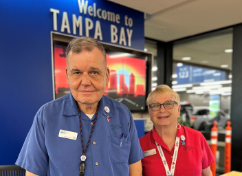 Male and female TPA ambassadors smiling in front of Welcome to Tampa Bay sign