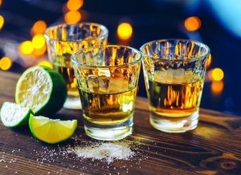 three shot glasses filled with tequila next to a sliced lime and salt