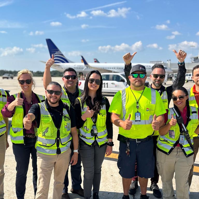 group of diverse workers in safety vests and safety clothing standing on airfield all giving the thumbs up gesture. standing on airfield